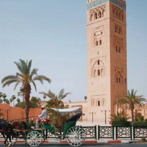 Traditional horse-drawn carriage in Marrakesh driving past palm trees and the historic Koutoubia Mosque minaret.