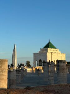 The majestic Mausoleum of Mohammed V and ancient stone columns of the Hassan Tower complex in Rabat, Morocco, with the modern Mohammed VI Tower standing tall in the background at sunset.