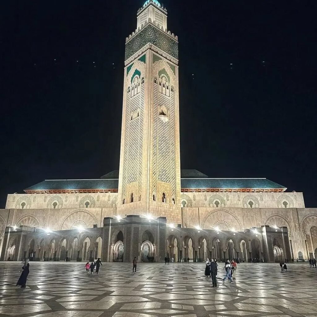 Grand Hassan II Mosque illuminated at night, showing its towering minaret and expansive paved courtyard in Casablanca, Morocco.