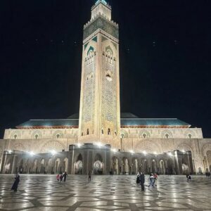 Grand Hassan II Mosque illuminated at night, showing its towering minaret and expansive paved courtyard in Casablanca, Morocco.