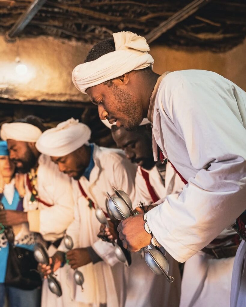 Gnawa music performers with qraqeb castanets beside a Moroccan flag