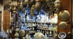 Intricate handcrafted brass and silver Moroccan lanterns, hanging lamps, and engraved decorative plates displayed outside a traditional shop in a bustling medina souk.