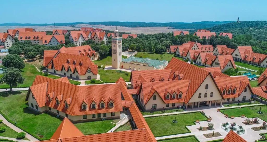 Aerial view of Al Akhawayn University campus in Ifrane, Morocco, featuring alpine-style architecture with red-tiled roofs, a central mosque tower, and manicured green lawns.