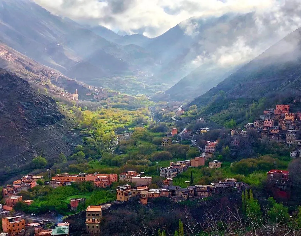 Picturesque mountain valley view of the Berber village of Imlil in the High Atlas Mountains of Morocco, featuring traditional earthen architecture surrounded by lush green terraced fields and dramatic peaks.