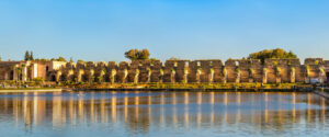 Scenic view of the historic Heri es-Souani granary and royal stables walls reflected in the tranquil waters of the Agdal Basin in Meknes, Morocco, under a clear sky.