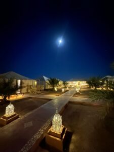 Desert camp lit up at night under the moon in Merzouga