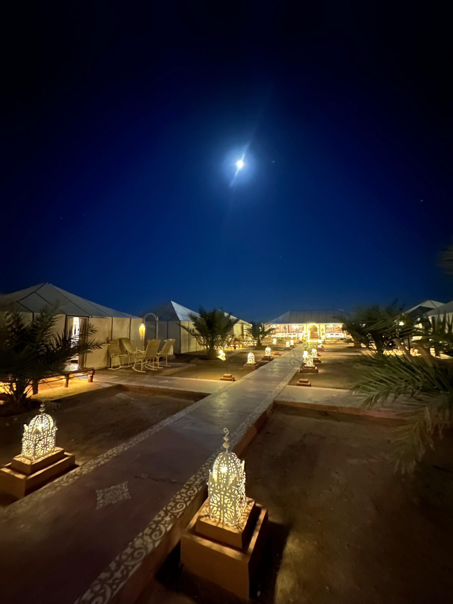 Desert camp lit up at night under the moon in Merzouga