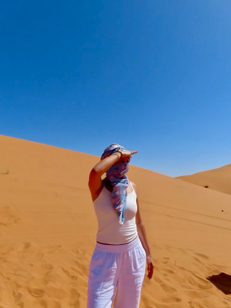 Student in a blue scarf shading her eyes on a Sahara dune near Merzouga