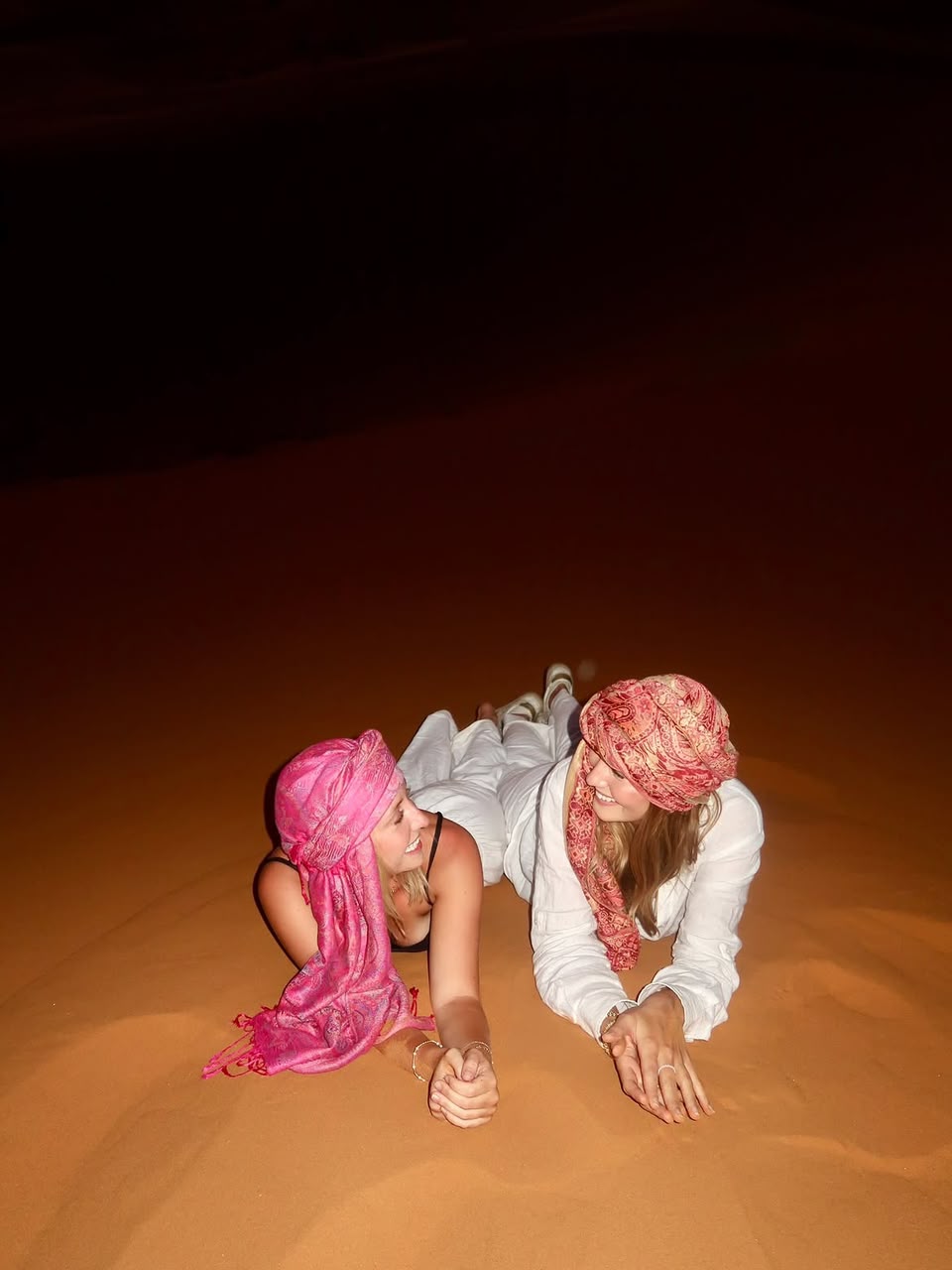 Two students lying on a Sahara dune at night wearing pink desert scarves