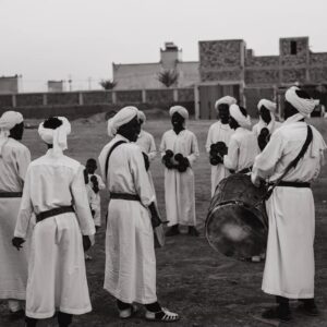 Gnawa musicians in white robes and turbans gathering with a drum in the Khamlia Gnawa village near Merzouga
