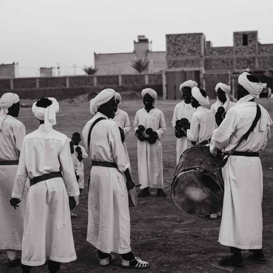Gnawa musicians in white robes and turbans gathering with a drum in Khamlia