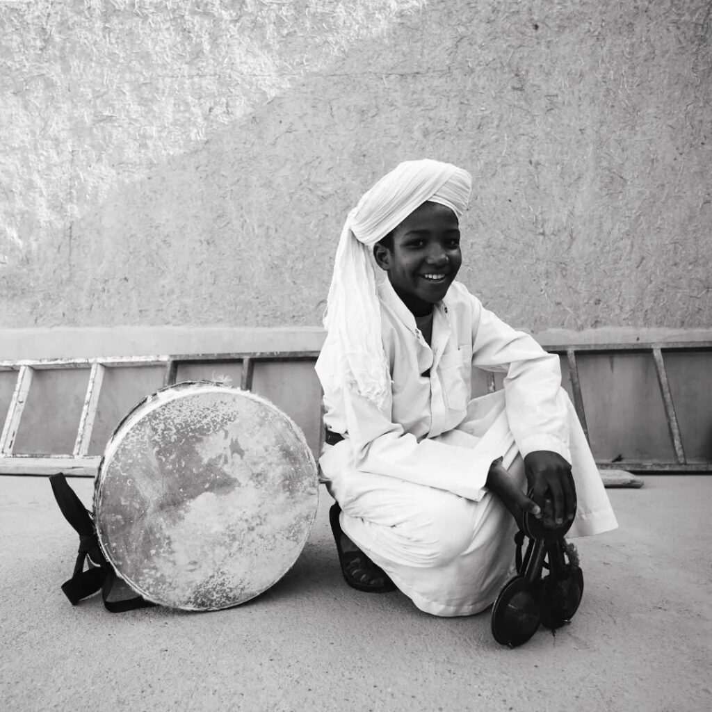 Young Gnawa musician smiling beside his frame drum in Khamlia