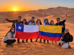 Grupo de viajeros con las banderas de Chile y Colombia al atardecer en las dunas del Sahara