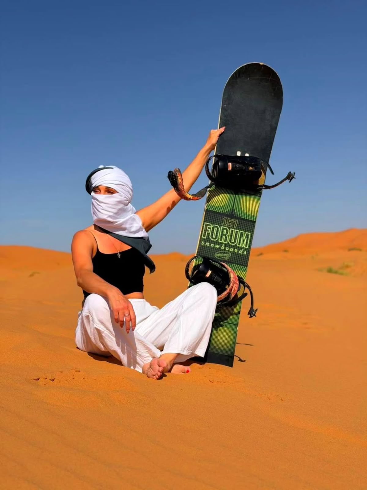 Traveler with a sandboard sitting on an orange dune in Merzouga, Morocco