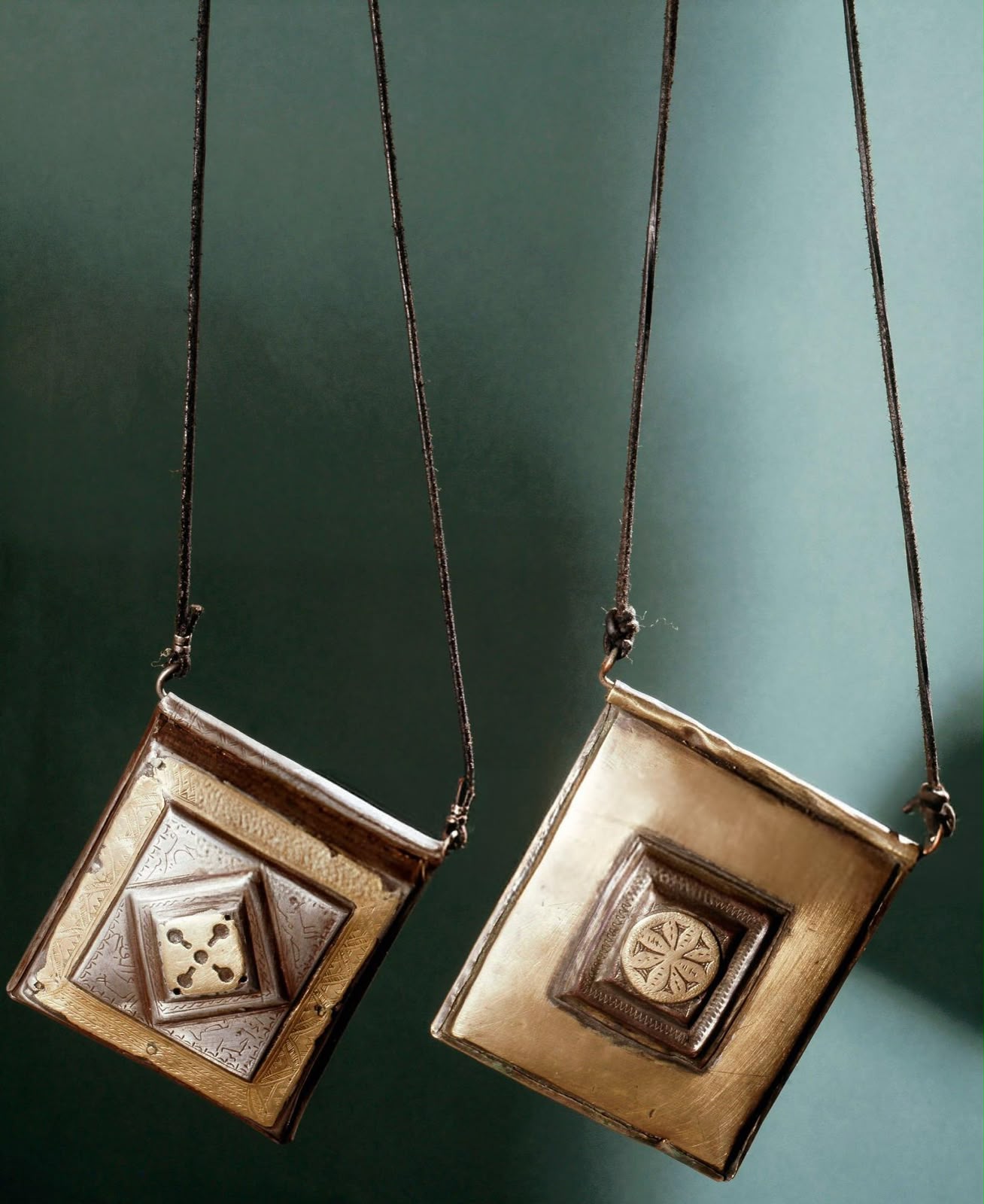 Two square metal amulet pendants hanging on cords