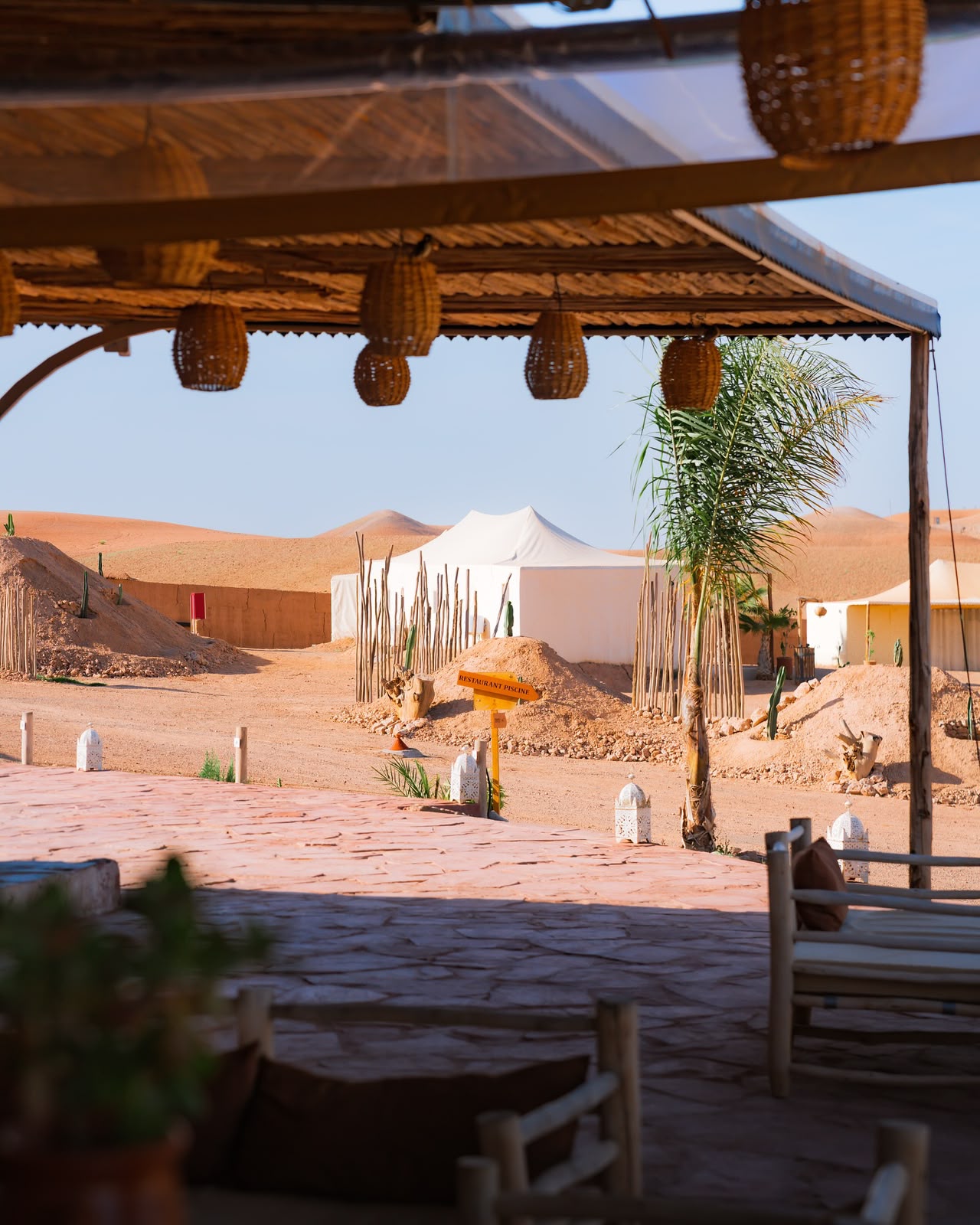 White tents and a shaded terrace with hanging wicker lamps at a camp