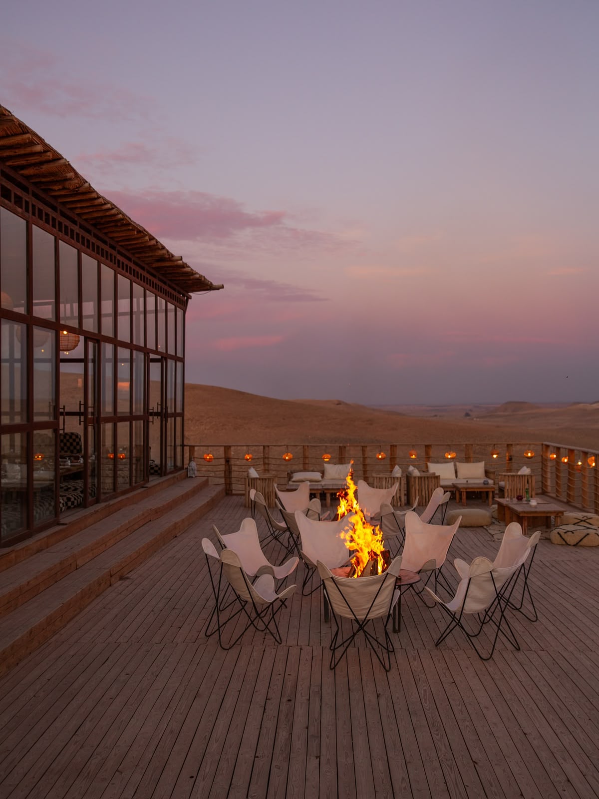 Fire pit and chairs on a wooden terrace at dusk under a pink sky