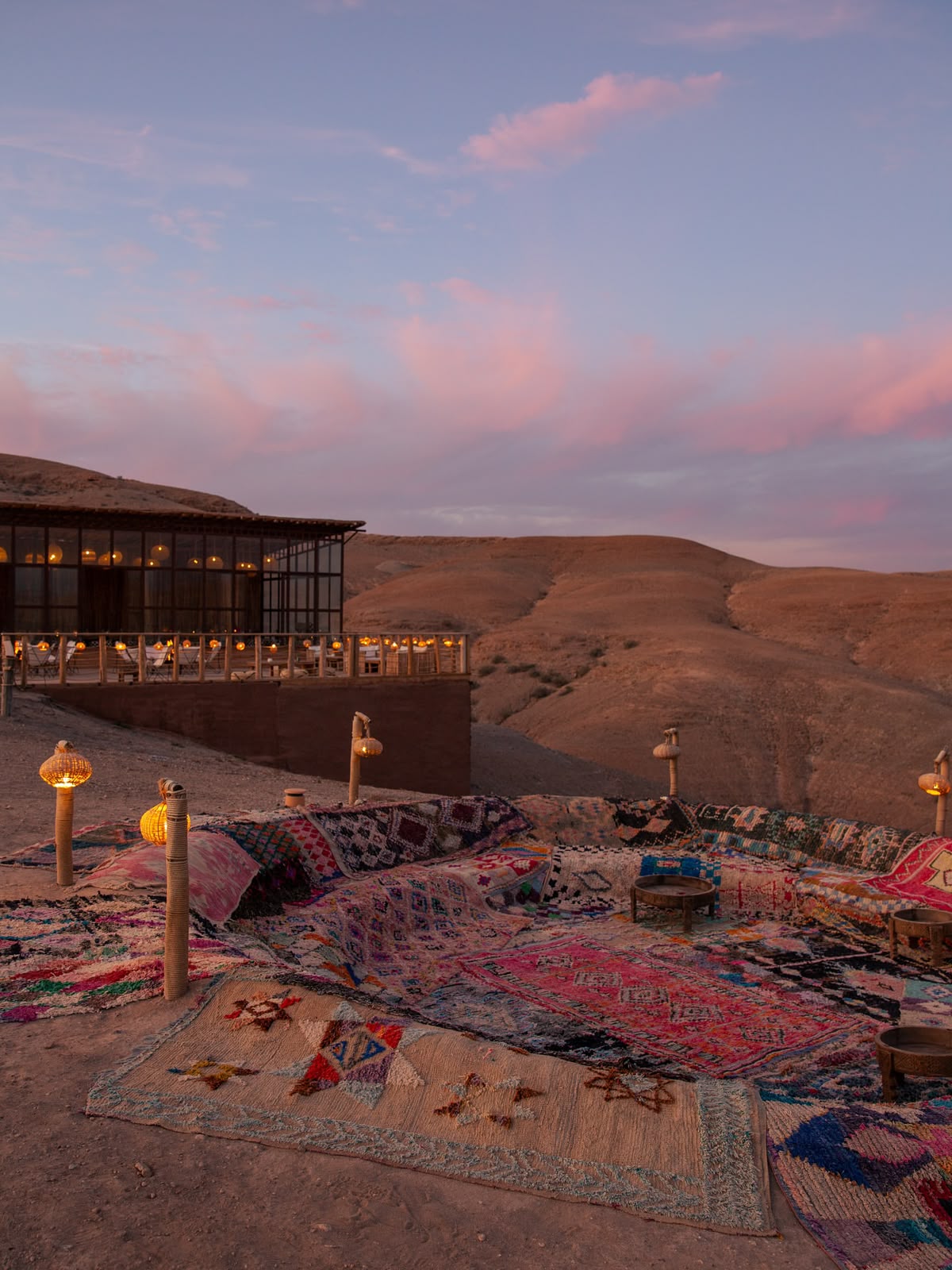 Lantern-lit lounge with Berber rugs and cushions at a camp in the Agafay Desert at dusk