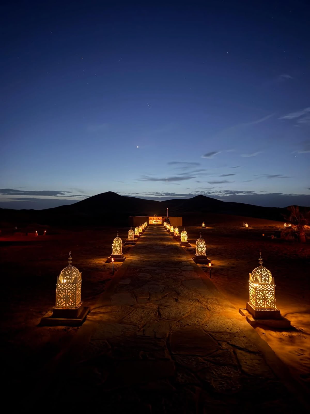 Lanterns lighting the path to a desert camp at dusk