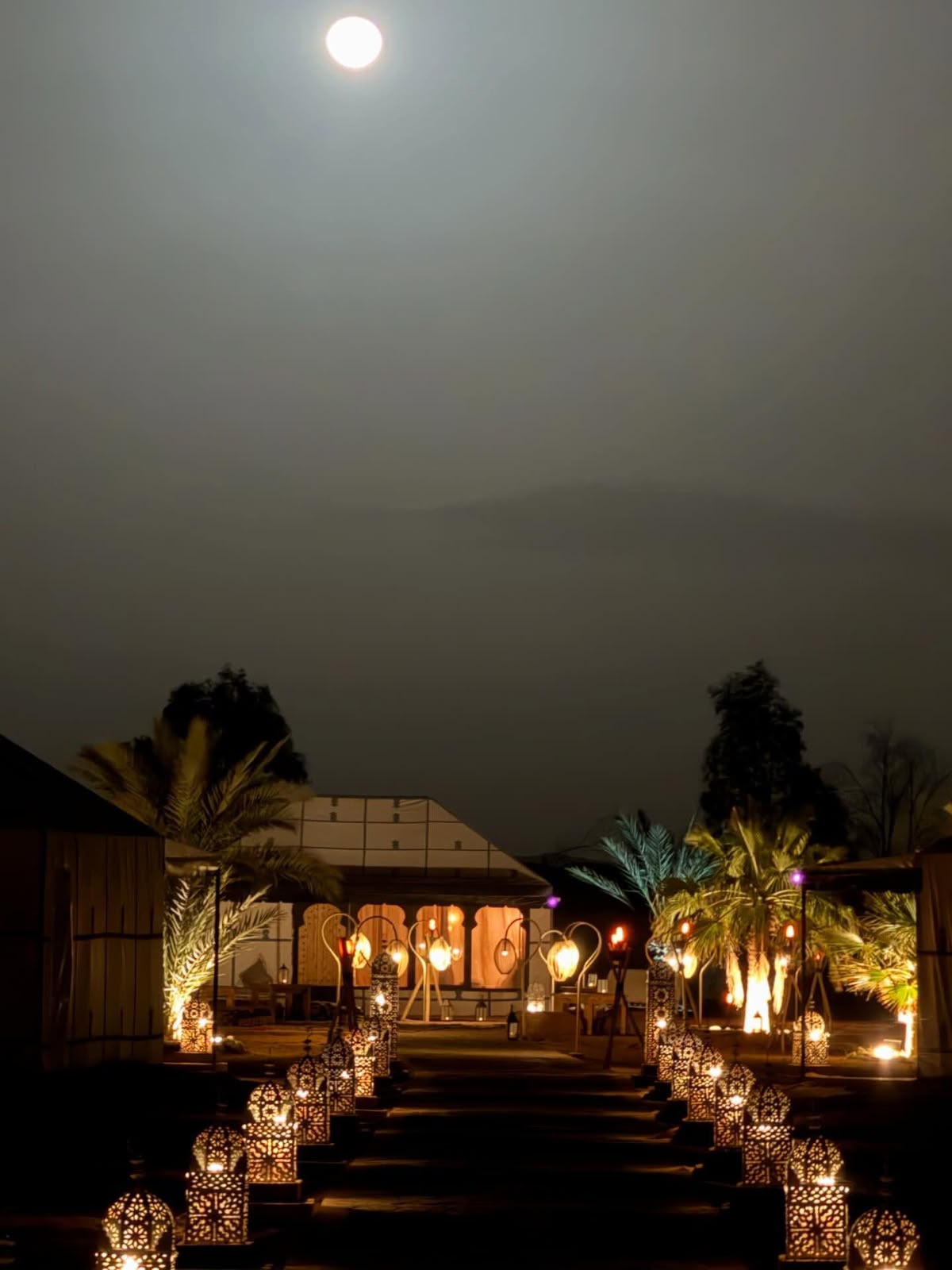 Full moon over a lantern-lit path at a luxury desert camp in the Sahara