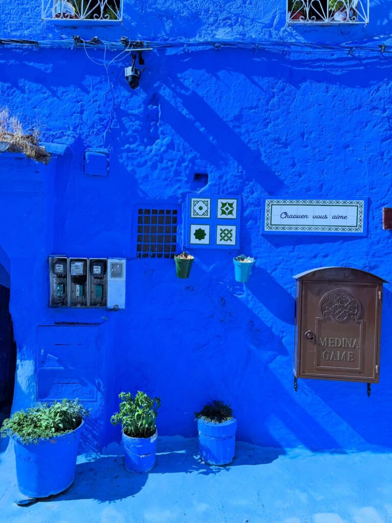 Pared azul de Chefchaouen con macetas, azulejos y un buzón antiguo