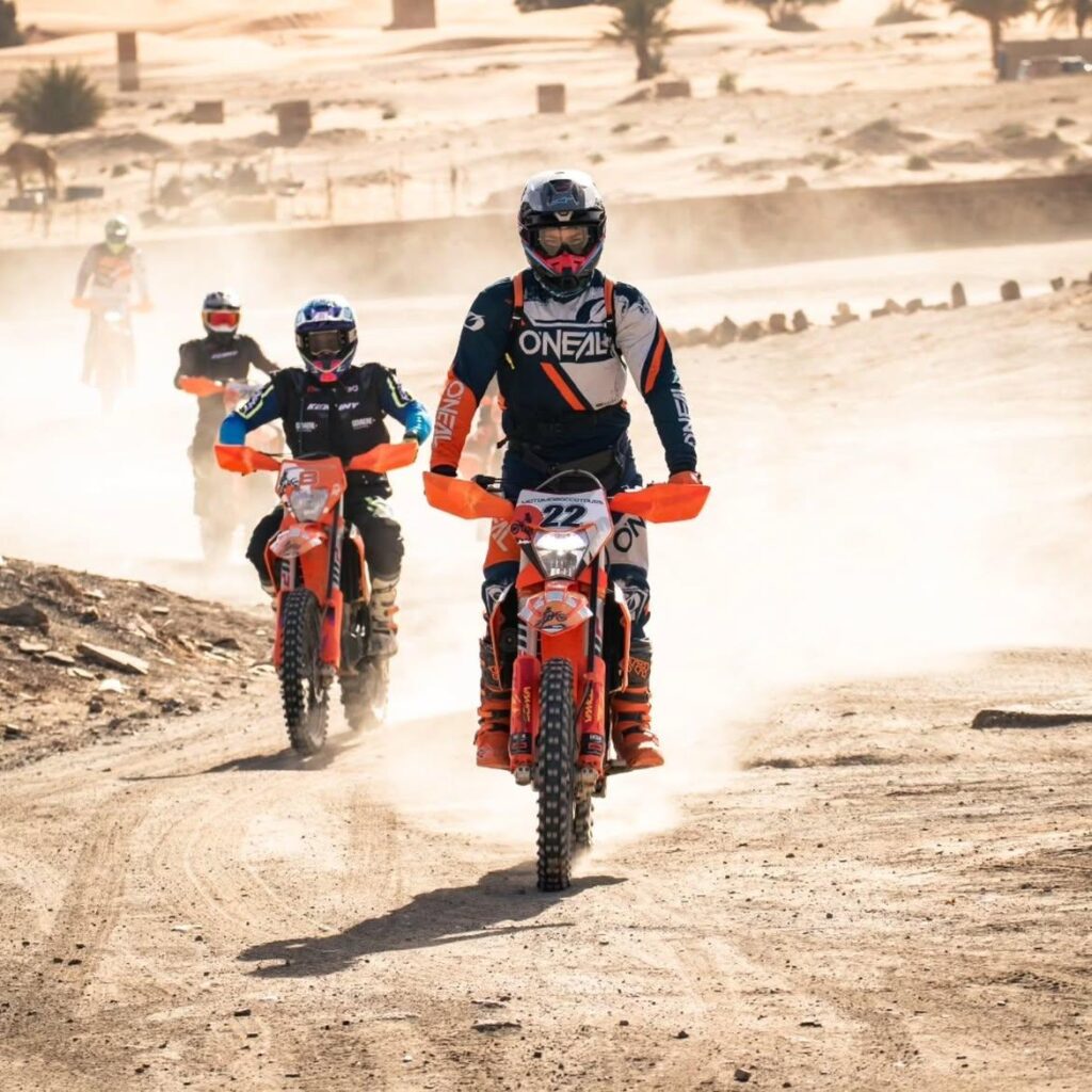Group of dirt bike riders crossing a dusty track near Merzouga