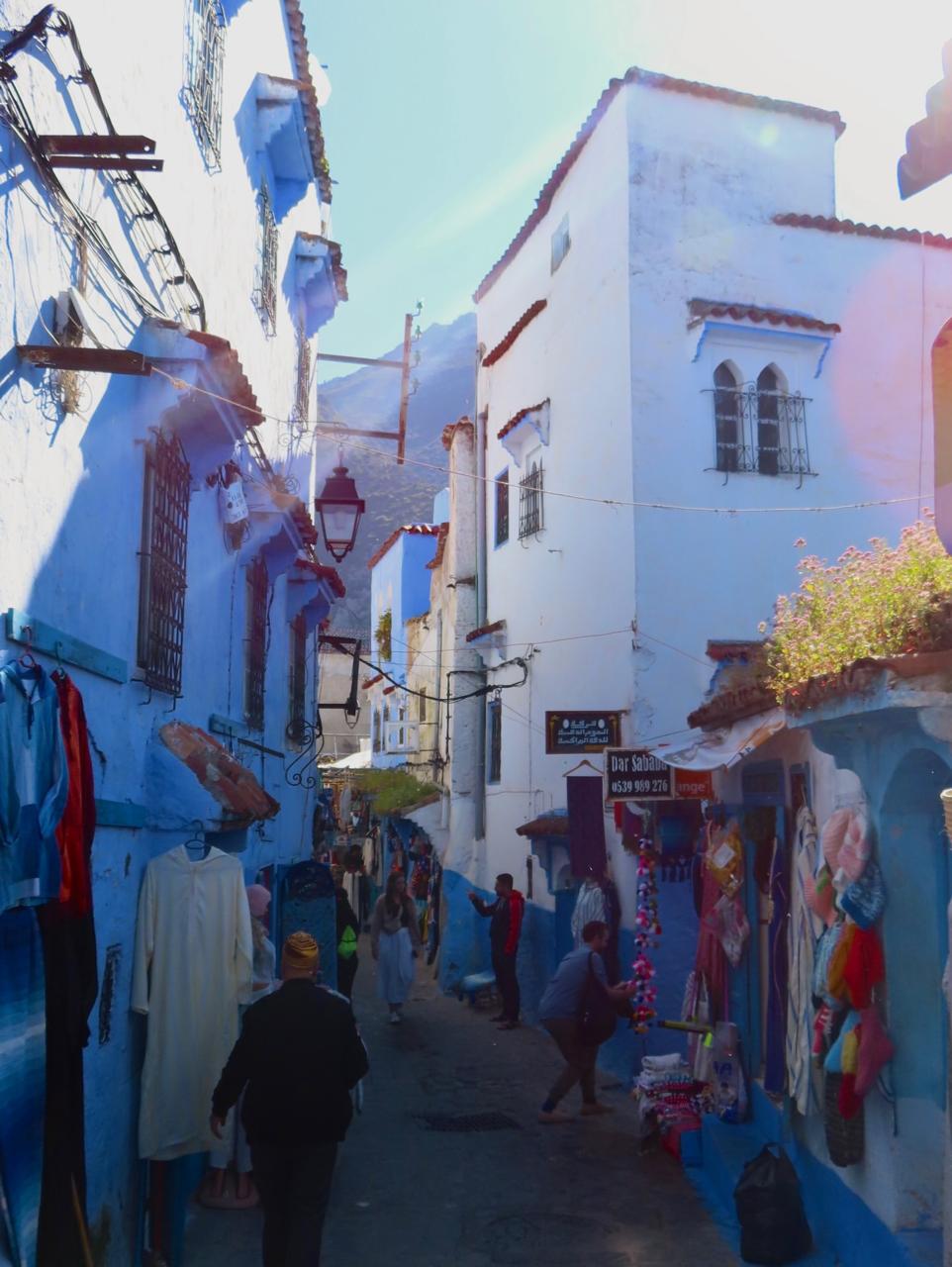 Narrow blue-painted alley with shops and people walking in Chefchaouen