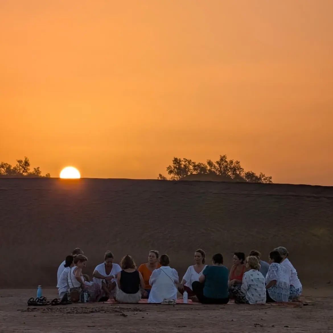 Group meditation circle on the dunes at sunset on a Sahara wellness retreat