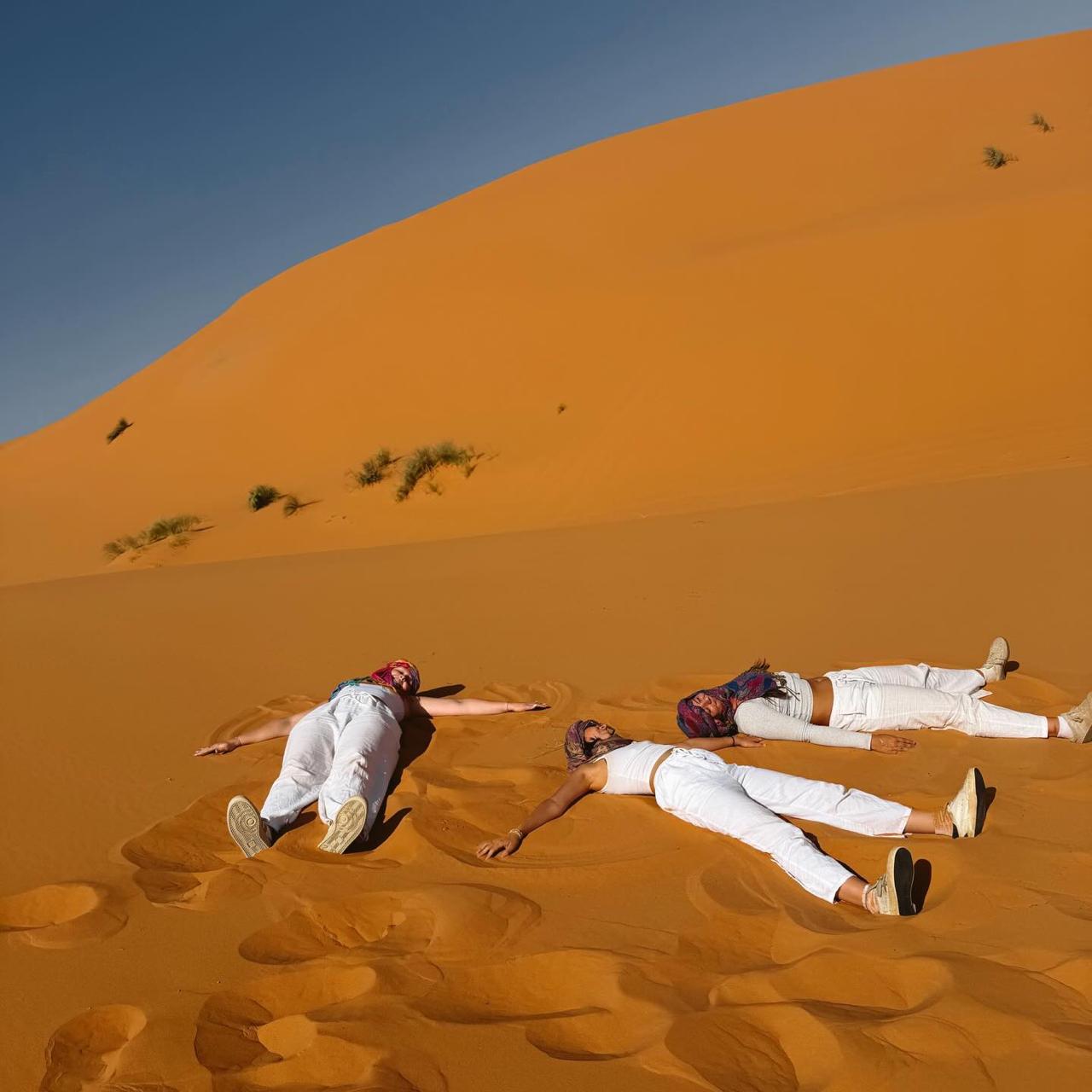 Two people lying on the orange sand of a Sahara dune