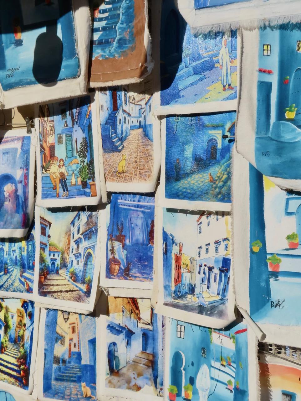 Market stall wall of small paintings and postcards of blue streets