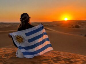 Viajera uruguaya con la bandera de Uruguay al atardecer en las dunas del Sahara