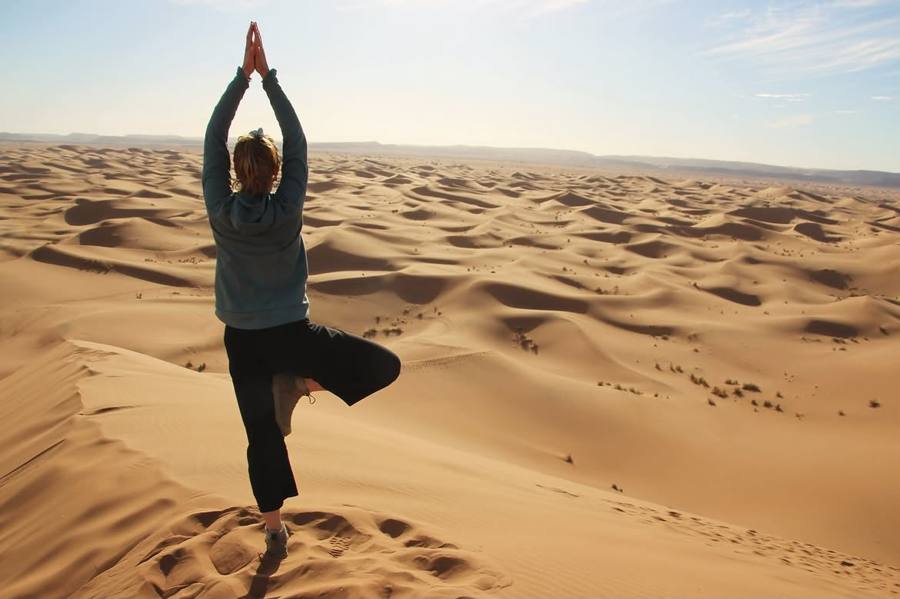 Woman in a yoga tree pose on a Sahara dune on a wellness tour in Morocco