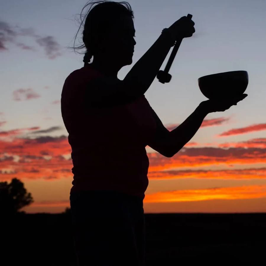 Woman playing a singing bowl at sunset during a desert meditation
