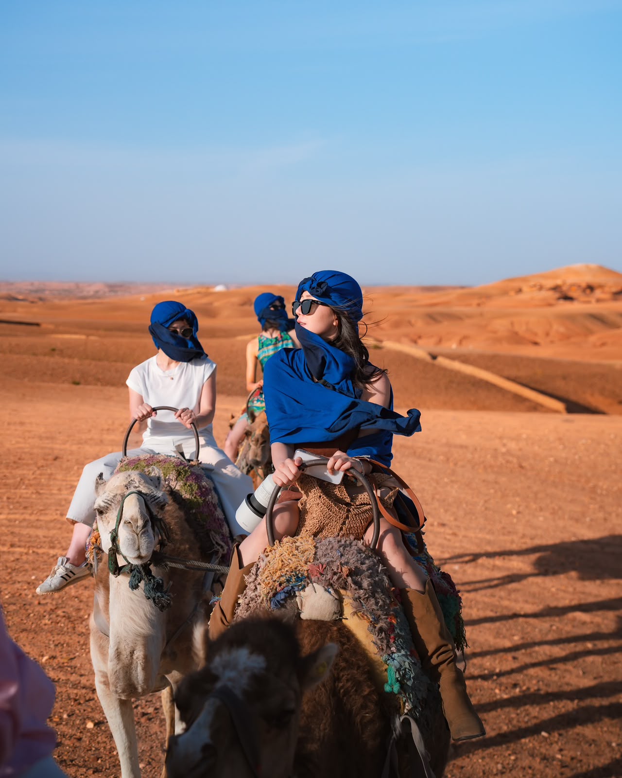 Travelers in blue desert scarves riding camels across the stony hills of the Agafay Desert