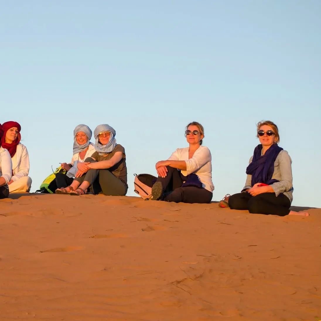 Travelers sitting together on a dune during a desert wellness retreat