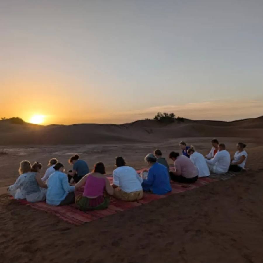Travelers watching the Sahara sunset on rugs during a wellness tour in Morocco