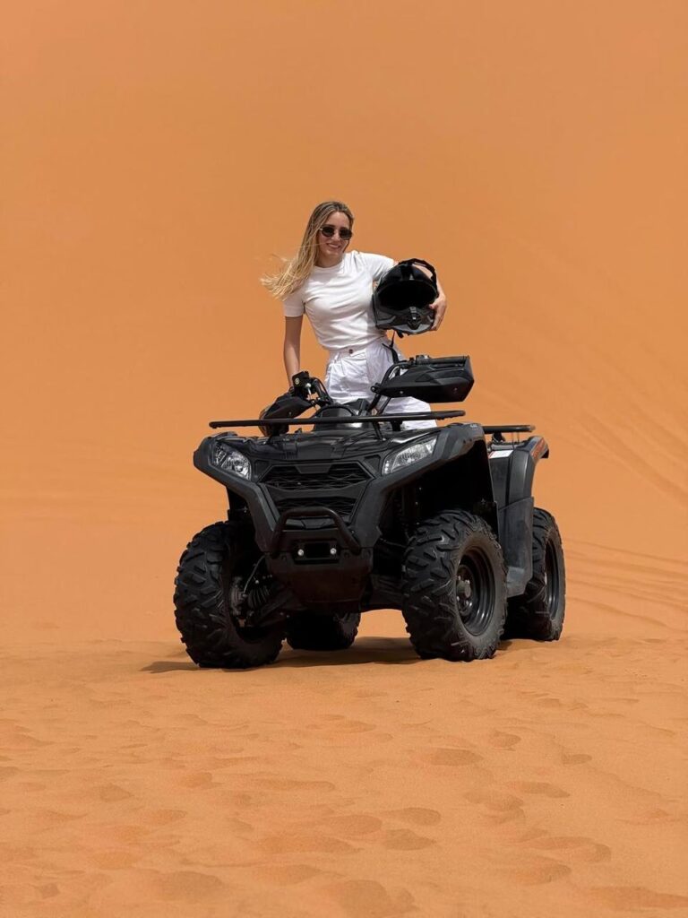 Smiling traveler holding her helmet beside a quad bike on a Merzouga dune
