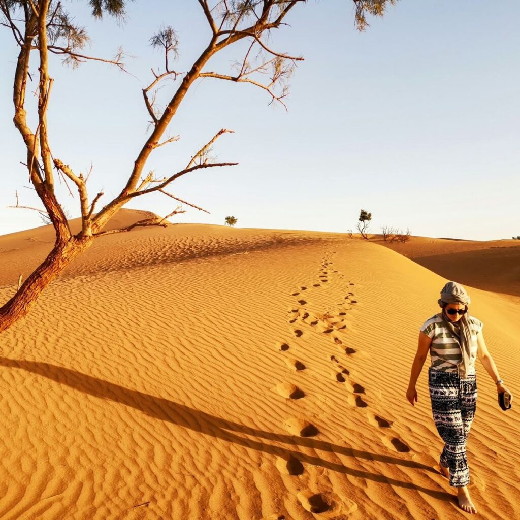 Woman walking barefoot across a Sahara dune leaving footprints