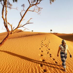 Woman walking barefoot across a Sahara dune leaving footprints