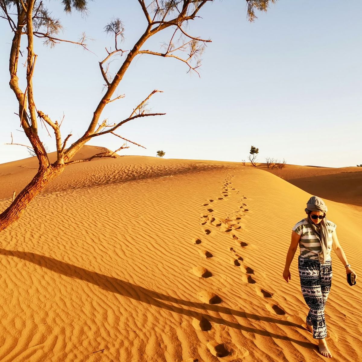 Woman walking barefoot across a Sahara dune leaving footprints